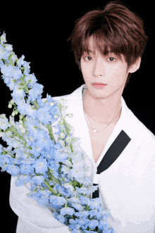 a young man in a white jacket is holding a bunch of blue flowers