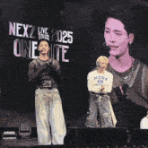 two men stand on a stage in front of a screen that says nex2 live tour 2025 onelite