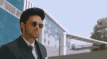 a man in a suit and tie wearing sunglasses stands in front of a building .