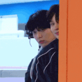 two young men peeking out from behind a wall