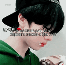 a boy wearing a green hoodie and a black hat is eating a piece of cake