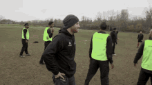 a man wearing a black hoodie with the letter k on it stands in a field with other men