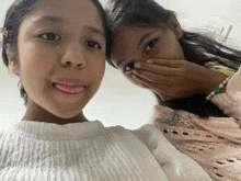 two girls are posing for a picture and one girl is covering her mouth with her hand