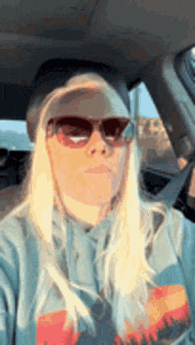 a blonde woman wearing sunglasses and a hat is sitting in a car .