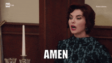 a woman sitting at a table with a candle and the word amen on the screen