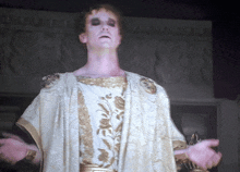 a man in a white and gold robe is standing with his arms outstretched in front of a wall