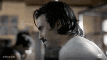 a man with long hair and a mustache is standing in a room and looking over his shoulder .