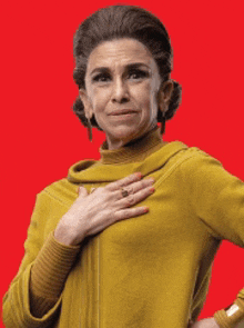 a woman in a yellow sweater has her hand on her chest and a ring on her finger