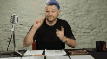 a man with blue hair is sitting at a desk in front of a microphone pointing up