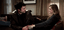 a man and a woman are sitting on a couch holding hands and looking at each other
