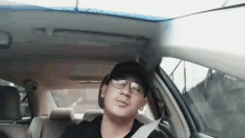 a man is sitting in the driver 's seat of a car wearing glasses and a hat .
