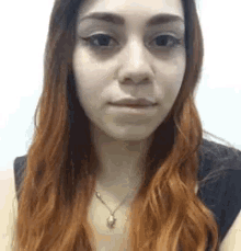 a woman with long red hair is wearing a necklace and a black shirt .