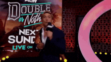 a man in a suit is holding a microphone in front of a sign that says double or nothing next sun .