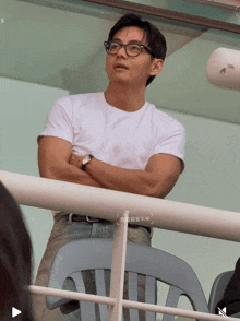 a man wearing glasses and a watch stands behind a railing with chinese writing on it