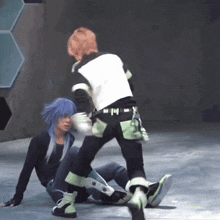 a man with blue hair is laying on the ground while another man stands up