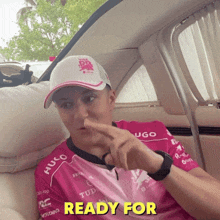 a man wearing a pink shirt that says hugo is sitting in a car