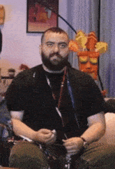 a man with a beard is sitting on a couch in front of a crash bandicoot mask .