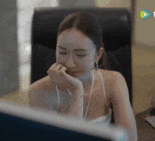 a woman is sitting in front of a computer screen with a play button on the bottom right