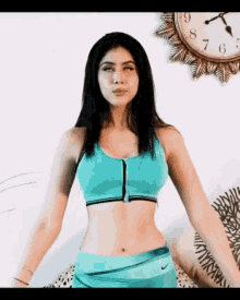 a woman in a blue sports bra is standing in front of a clock with the hands on the numbers 7 and 8