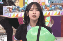 a girl is holding a green balloon in her hand and making a funny face .