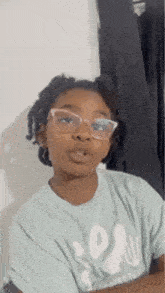 a young girl wearing glasses and a light blue t-shirt is making a funny face .