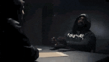 a man in a hoodie talks to a woman while sitting at a table