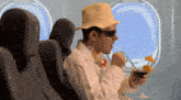 a man wearing a hat and sunglasses is drinking from a straw