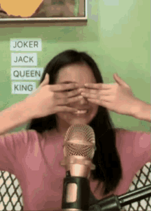 a woman is covering her eyes in front of a microphone while smiling .