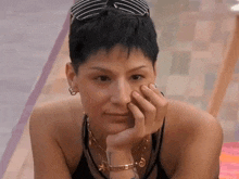 a woman with short hair wearing sunglasses and a necklace is sitting with her hand on her face .