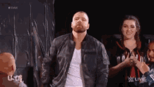 a man in a leather jacket is standing in front of a crowd in a dark room .