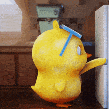 a yellow chicken with a blue straw on its head is standing next to a fridge