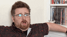 a man with glasses and a beard is standing in front of a bookshelf with a book titled joe hitch