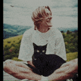 a man in a white shirt is sitting with his legs crossed and a black cat on his lap