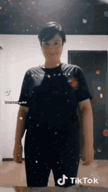 a woman wearing a black t-shirt and black pants is standing in front of a door with tik tok written on the bottom