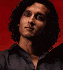 a man with curly hair is wearing a black shirt and looking at the camera