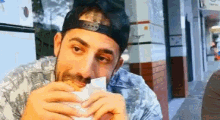 a man wearing a hat is eating a hamburger