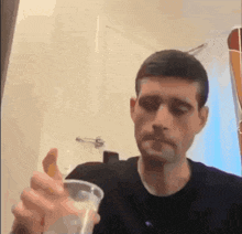 a man in a black shirt is holding a cup of liquid in his hand .