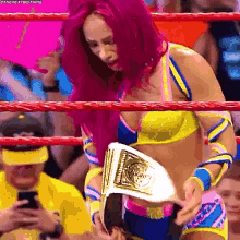 a woman with pink hair is in a wrestling ring holding a championship belt .