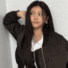 a woman with long black hair is leaning against a wall with her hand in her hair .