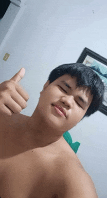 a young man without a shirt is giving a thumbs up sign .