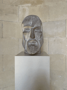 a statue of a man with a beard is on a pedestal in front of a brick wall