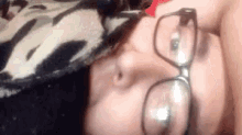 a woman wearing glasses is laying on a bed with a cow print blanket .