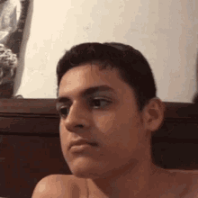 a young man is sitting on a bed without a shirt on and making a funny face .