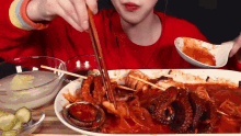 a woman is eating a plate of food with chopsticks and a bowl of sauce .
