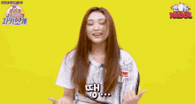 a girl with long hair is standing in front of a yellow background and holding her hair .