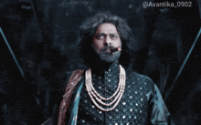 a man with a beard is wearing a pearl necklace and smoking a cigar in a dark room
