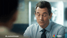 a man in a suit and tie talks to another man with the nbc logo on the bottom right