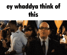 a man in a suit and tie is standing in front of a crowd of people and says ey whaddya think of this .