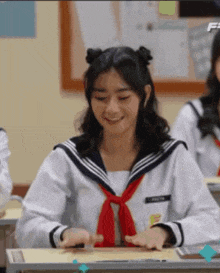 a girl in a sailor uniform sits at a desk in a classroom .