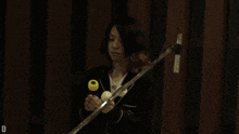 a person holding a microphone and a drum stick with the letter d visible in the corner